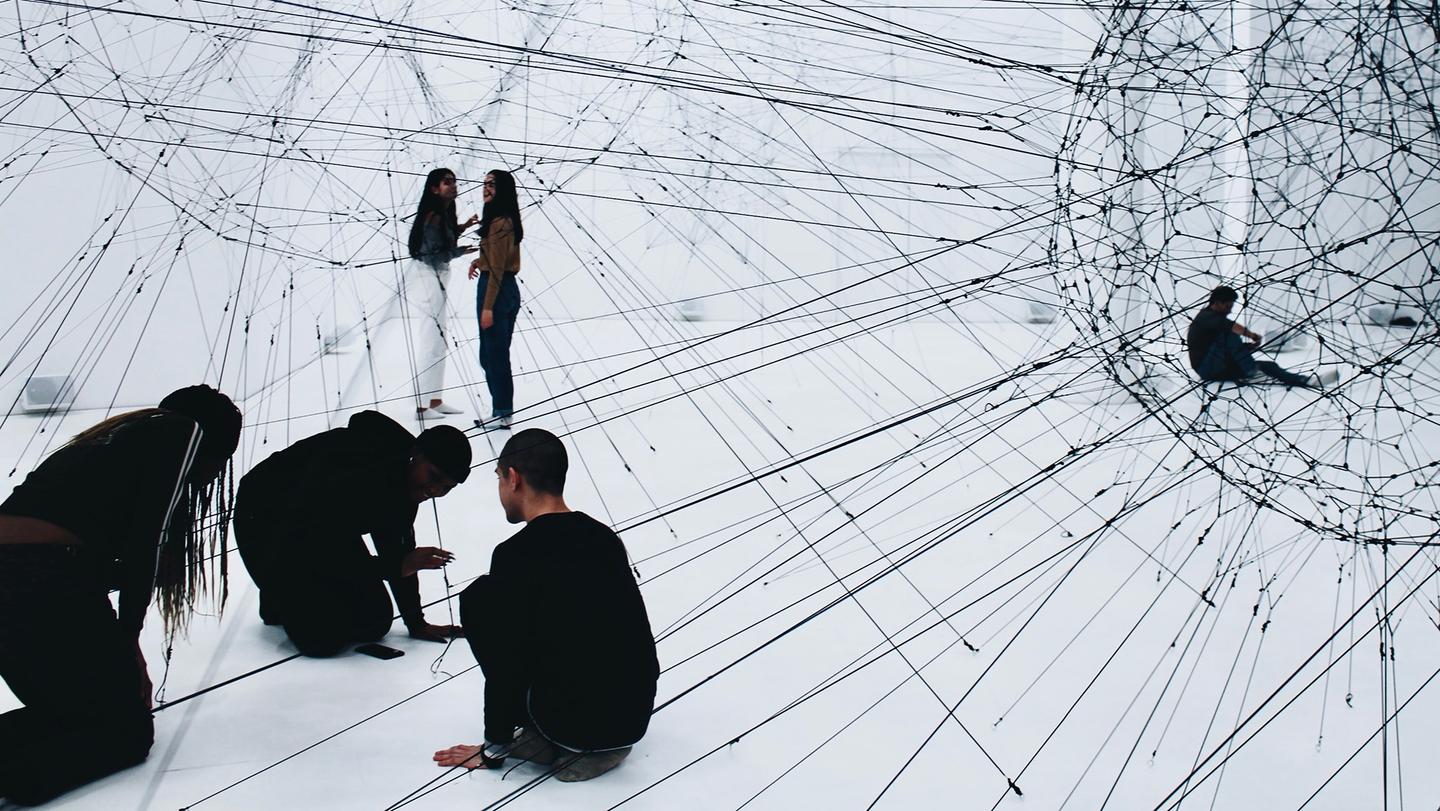 A group of young people exploring a contemporary art installation consisting of connected strings